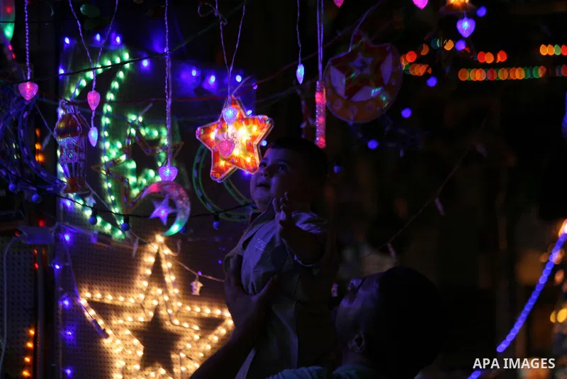 A Palestinian man carries his son as they play with festive lights decorated an alley in Jerusalem's old city with during the first day of Muslim holy month of Ramadan, June 29, 2014. Muslim believers abstain from eating...