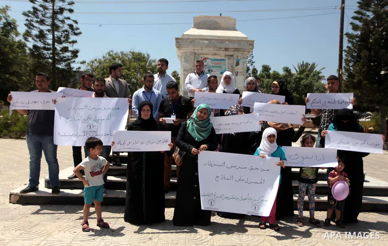 Palestinian relatives of cancer patients hold placards during a protest demanding for the opening of Rafah crossing border, in Gaza City on June 30, 2014. Photo by Ashraf Amra