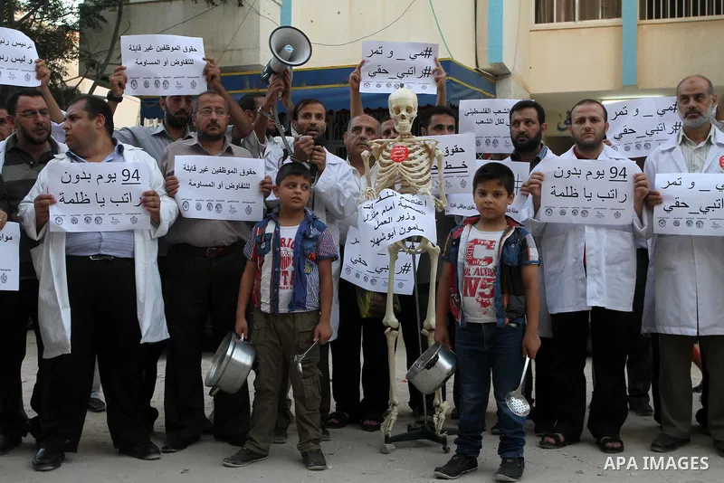 Palestinian employees of the former government in Gaza Strip hold placards during a protest against not receiving their salaries, in front of the home of Minister of Labor Mamoun Abu Shahla, in Gaza City on July 03, 2014...
