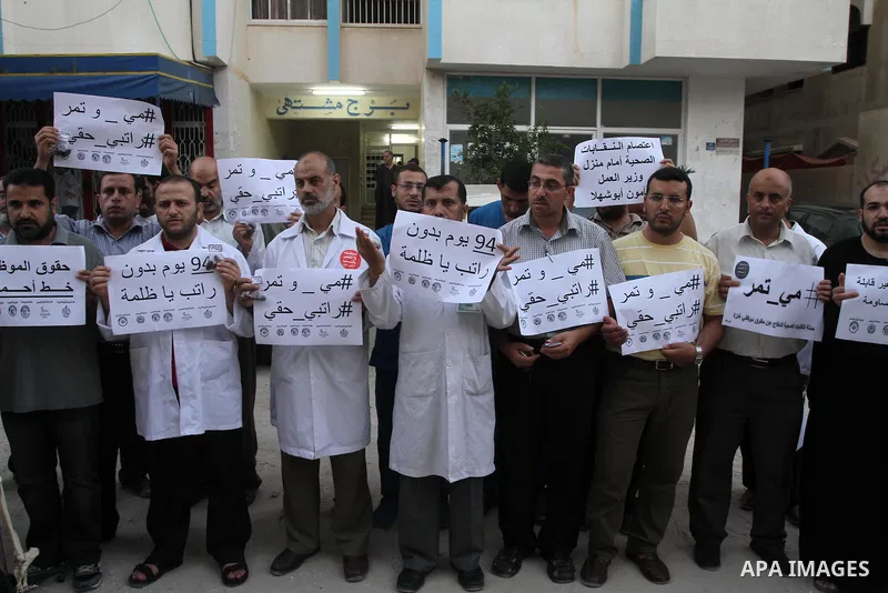 Palestinian employees of the former government in Gaza Strip hold placards during a protest against not receiving their salaries, in front of the home of Minister of Labor Mamoun Abu Shahla, in Gaza City on July 03, 2014...