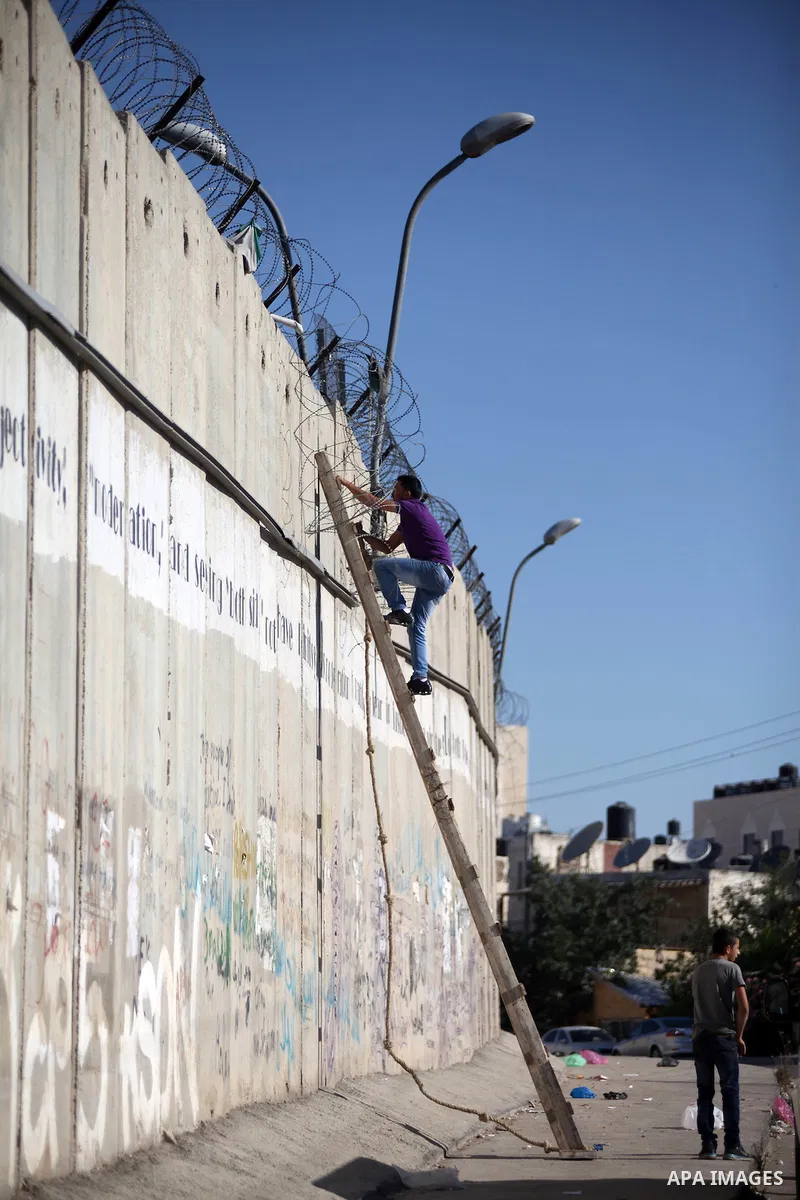 Palestinians use a ladder to climb over a section of Israel's separation barrier in the West Bank village of Al-Ram, as they try to avoid crossing Israeli-controlled checkpoints to reach the al-Aqsa mosque compound in Je...