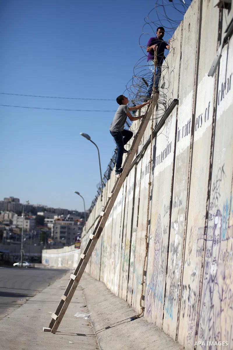 Palestinians use a ladder to climb over a section of Israel's separation barrier in the West Bank village of Al-Ram, as they try to avoid crossing Israeli-controlled checkpoints to reach the al-Aqsa mosque compound in Je...