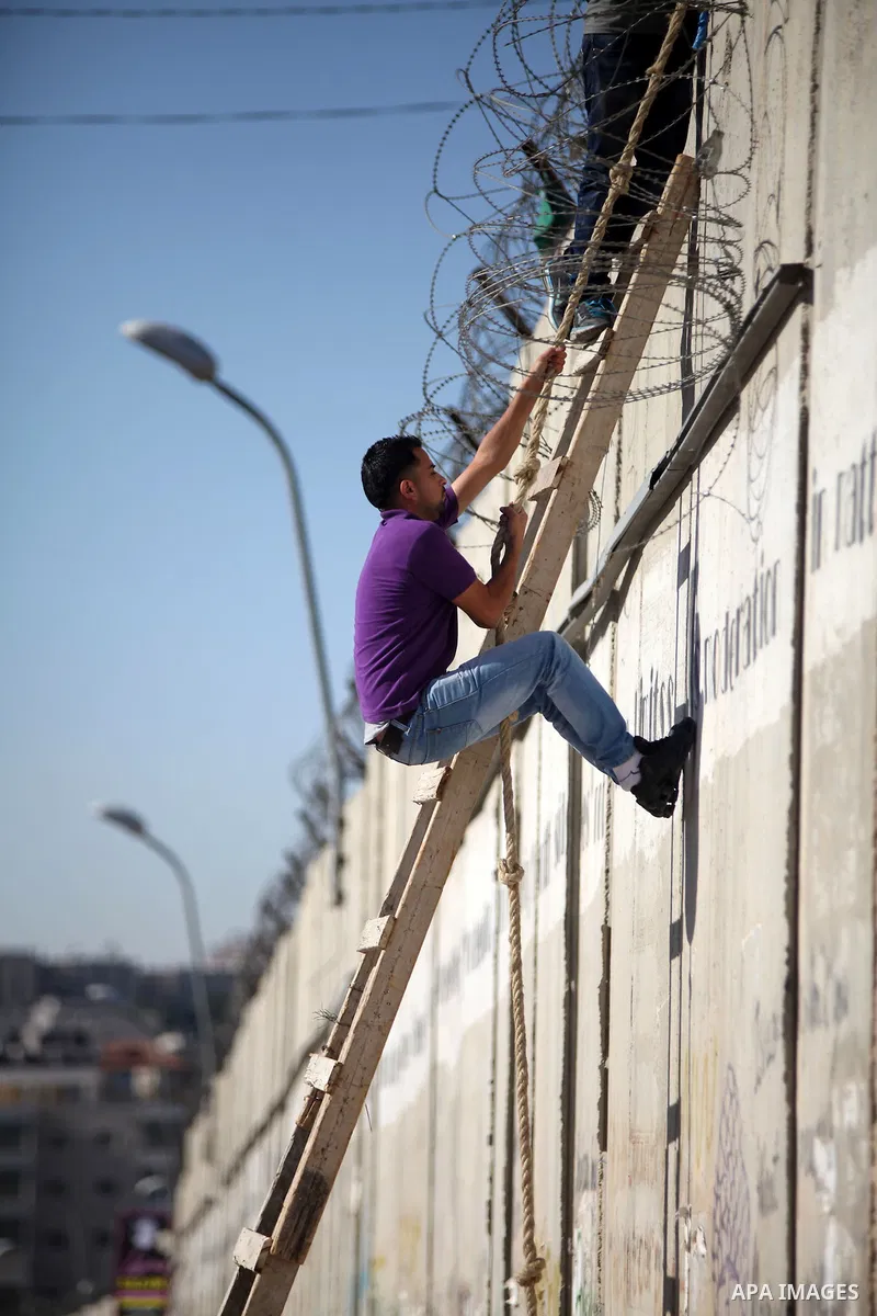 A Palestinian uses a ladder to climb over a section of Israel's separation barrier in the West Bank village of Al-Ram, as they try to avoid crossing Israeli-controlled checkpoints to reach the al-Aqsa mosque compound in...