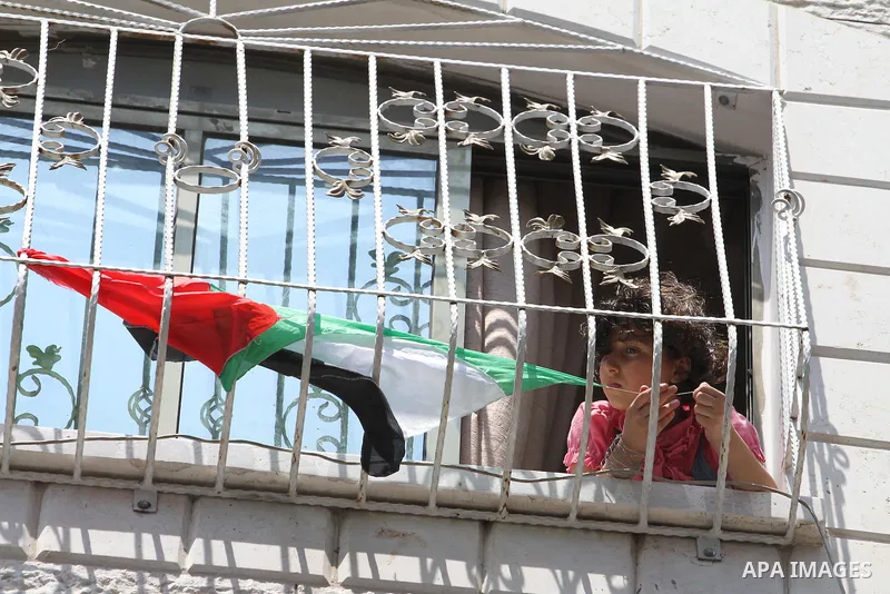 A Palestinian girl looks from he family's house window at Hamas movement supporters during a rally in solidarity with the Palestinian in the West Bank and against any possible Israeli attack on Gaza, in Jabalia in the no...