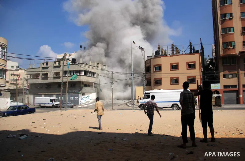 Palestinians watch as smoke rises from a destroyed building following an Israeli air strike at al-Shatee refugee camp, in Gaza City on July 21, 2014. The Palestinian death toll in an Israeli offensive in the Gaza Strip j...