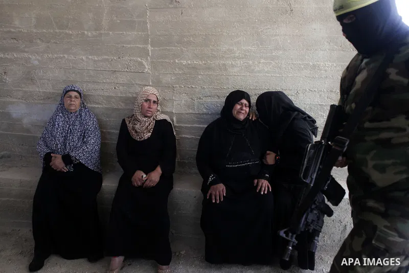 A Palestinian gunman walks past relatives of Mahmoud al-Shawamreh during his funeral in the West Bank town of Al-Ram near Jerusalem July 22, 2014. Israeli troops shot dead al-Shawamreh during clashes with stone-throwers...