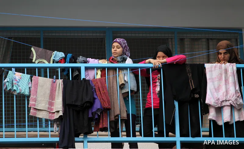 A displaced Palestinian woman with her daughters look on as others attend the Eid al-Fitr prayer at a United Nations school, in Gaza City on July 28, 2014. The U.N. Security Council agreed on a statement on Sunday urging...