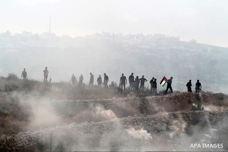 Palestinian protesters wave their national flag during clashes with Israeli security forces following the Eid al-Fitr prayer in a protest against the Israeli military operation on Gaza Strip, in the West Bank villages of...