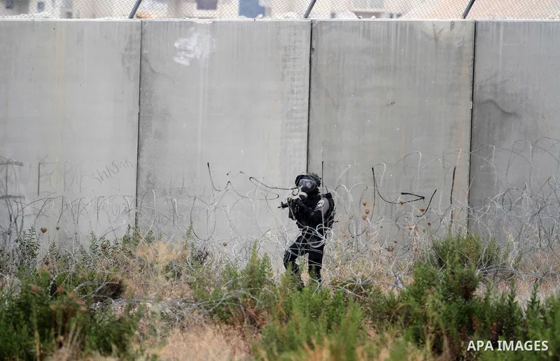An Israeli soldiers fires tear gas at Palestinian protesters during clashes in following the Eid al-Fitr prayer in a protest against the Israeli military operation on Gaza Strip, in the West Bank villages of Bilin, near...