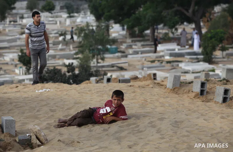 A Palestinian boy sits next to the grave of a relative, who medics said was killed during the Israeli offensive, on the Muslim holiday of Eid al-Fitr at a cemetery in Beit Lahiyah in the northern Gaza Strip July 28, 2014...