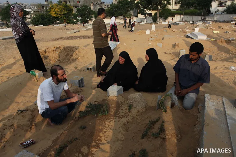 A Palestinian woman (2nd R) mourns next to her son's grave, who medics said was killed during the Israeli offensive, during the Muslim holiday of Eid al-Fitr at a cemetery in Beit Lahiyah in the northern Gaza Strip July...