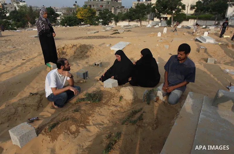 A Palestinian woman (2nd R) mourns next to her son's grave, who medics said was killed during the Israeli offensive, during the Muslim holiday of Eid al-Fitr at a cemetery in Beit Lahiyah in the northern Gaza Strip July...