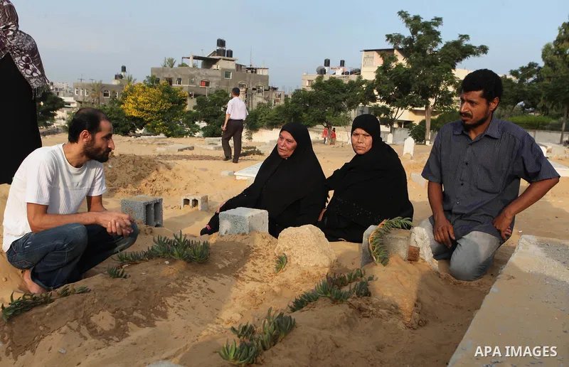 A Palestinian woman (2nd R) mourns next to her son's grave, who medics said was killed during the Israeli offensive, during the Muslim holiday of Eid al-Fitr at a cemetery in Beit Lahiyah in the northern Gaza Strip July...