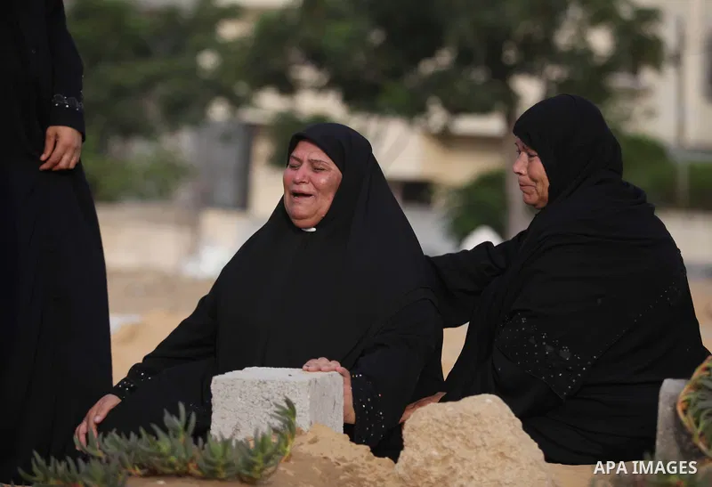 A Palestinian woman (2nd R) mourns next to her son's grave, who medics said was killed during the Israeli offensive, during the Muslim holiday of Eid al-Fitr at a cemetery in Beit Lahiyah in the northern Gaza Strip July...