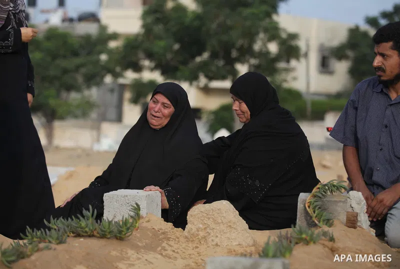 A Palestinian woman (2nd R) mourns next to her son's grave, who medics said was killed during the Israeli offensive, during the Muslim holiday of Eid al-Fitr at a cemetery in Beit Lahiyah in the northern Gaza Strip July...