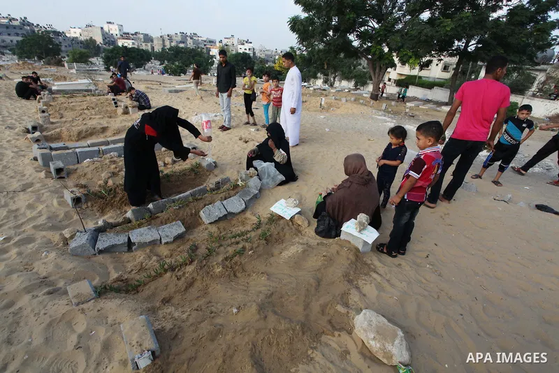 Palestinians mourn at the graves of their relatives, who medics said were killed during the Israeli offensive, during the Muslim holiday of Eid al-Fitr at a cemetery in Beit Lahiyah in the northern Gaza Strip July 28, 20...