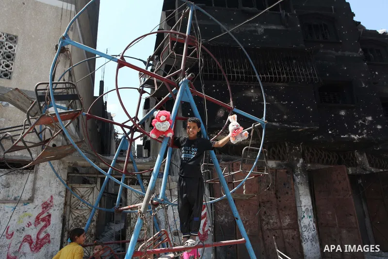 Palestinian children play near a damaged mini ferris wheel in the wartorn Shejaiya district of Gaza City on July 28, 2014 on the first day of Eid al-Fitr holiday. The Muslim three-day Eid al-Fitr festival, that marks the...