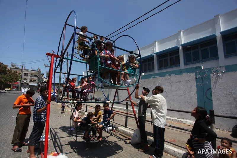Palestinian children play on a mini ferris wheel outside an United Nations (UN) school in Jabalia in the northern Gaza strip, on July 28, 2014, on the beginning of the Muslim Eid festival ending the month-long fast of Ra...