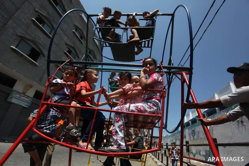 Palestinian children play on a mini ferris wheel outside an United Nations (UN) school in Jabalia in the northern Gaza strip, on July 28, 2014, on the beginning of the Muslim Eid festival ending the month-long fast of Ra...