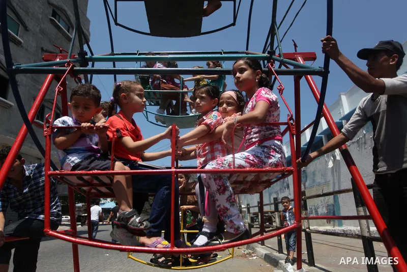 Palestinian children play on a mini ferris wheel outside an United Nations (UN) school in Jabalia in the northern Gaza strip, on July 28, 2014, on the beginning of the Muslim Eid festival ending the month-long fast of Ra...
