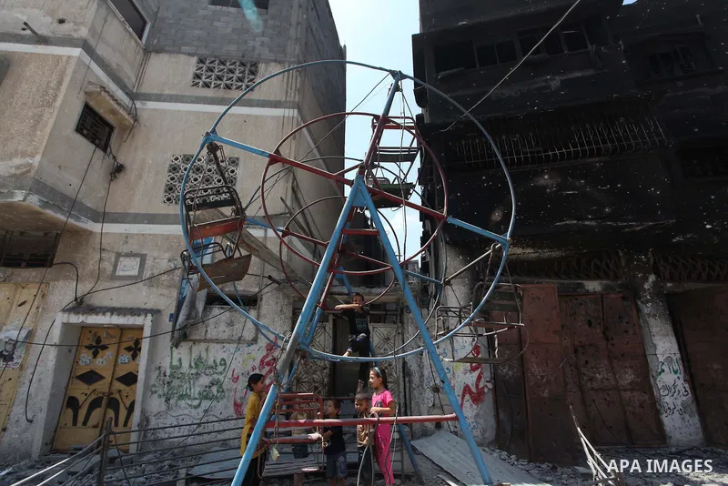 Palestinian children play near a damaged mini ferris wheel in the wartorn Shejaiya district of Gaza City on July 28, 2014 on the first day of Eid al-Fitr holiday. The Muslim three-day Eid al-Fitr festival, that marks the...