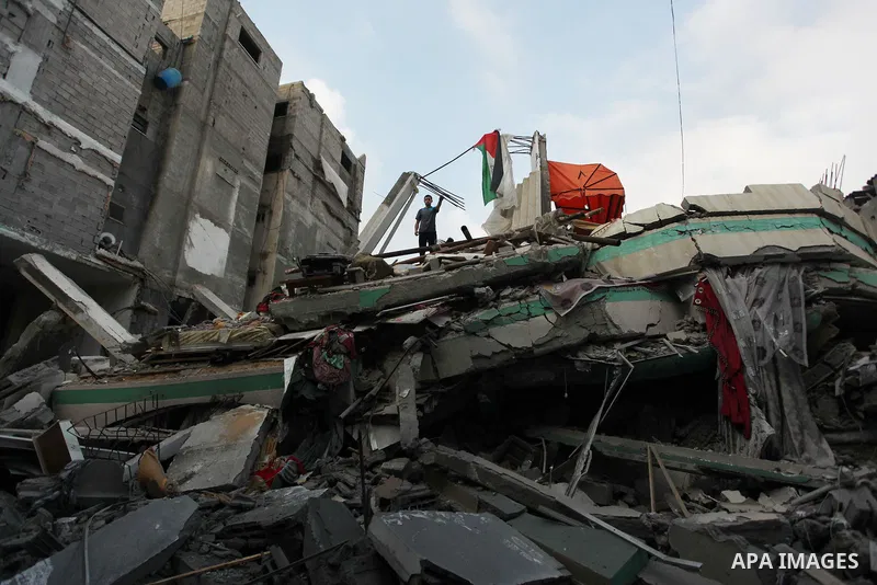 A Palestinian man displays national flags, Islamist Hamas movement flags and portraits of Hamas top leader in Gaza, Ismail Haniya, on the rubble of the latter's house after it was hit by an overnight Israeli air strike,...