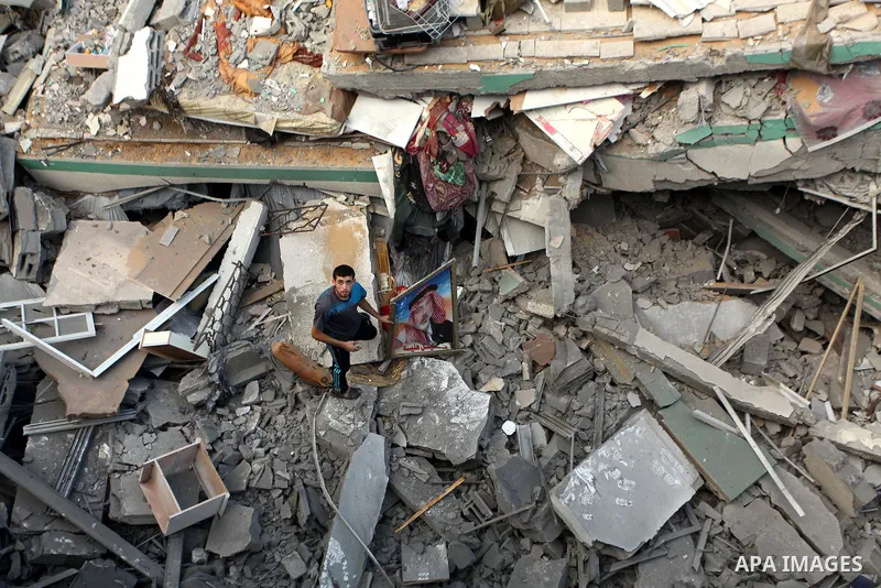 A Palestinian man displays national flags, Islamist Hamas movement flags and portraits of Hamas top leader in Gaza, Ismail Haniya, on the rubble of the latter's house after it was hit by an overnight Israeli air strike,...
