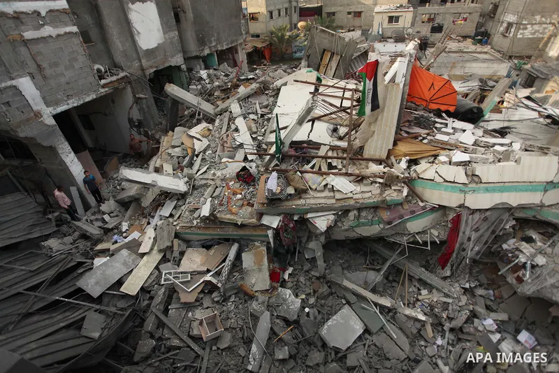 A Palestinian man displays national flags, Islamist Hamas movement flags and portraits of Hamas top leader in Gaza, Ismail Haniya, on the rubble of the latter's house after it was hit by an overnight Israeli air strike,...