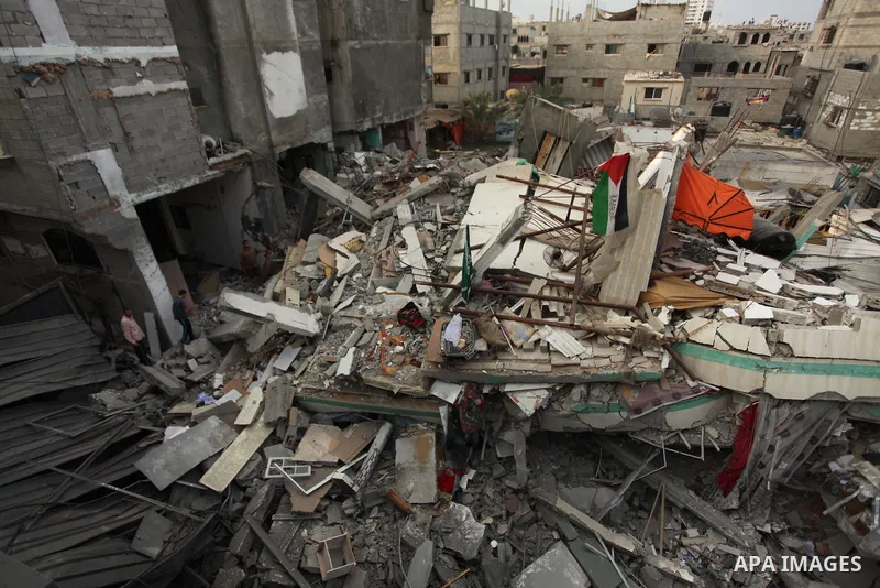 A Palestinian man displays national flags, Islamist Hamas movement flags and portraits of Hamas top leader in Gaza, Ismail Haniya, on the rubble of the latter's house after it was hit by an overnight Israeli air strike,...