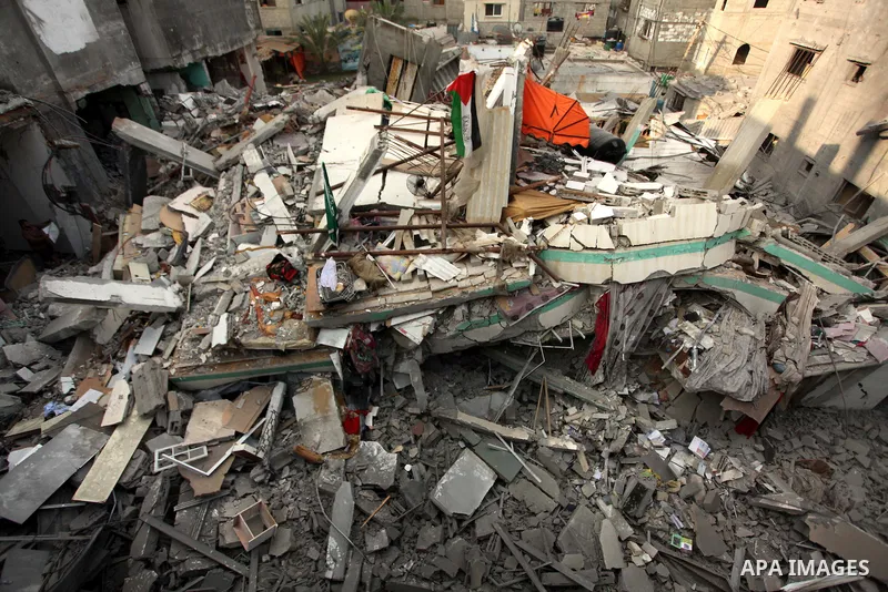 A Palestinian man displays national flags, Islamist Hamas movement flags and portraits of Hamas top leader in Gaza, Ismail Haniya, on the rubble of the latter's house after it was hit by an overnight Israeli air strike,...