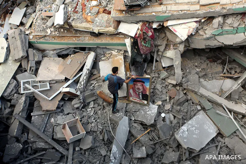 A Palestinian man displays national flags, Islamist Hamas movement flags and portraits of Hamas top leader in Gaza, Ismail Haniya, on the rubble of the latter's house after it was hit by an overnight Israeli air strike,...