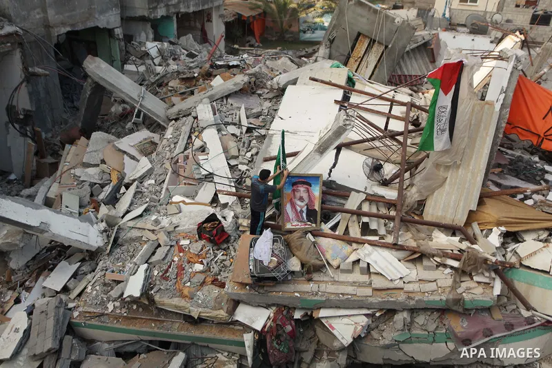 A Palestinian man displays national flags, Islamist Hamas movement flags and portraits of Hamas top leader in Gaza, Ismail Haniya, on the rubble of the latter's house after it was hit by an overnight Israeli air strike,...