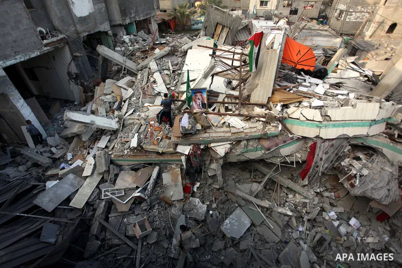 A Palestinian man displays national flags, Islamist Hamas movement flags and portraits of Hamas top leader in Gaza, Ismail Haniya, on the rubble of the latter's house after it was hit by an overnight Israeli air strike,...