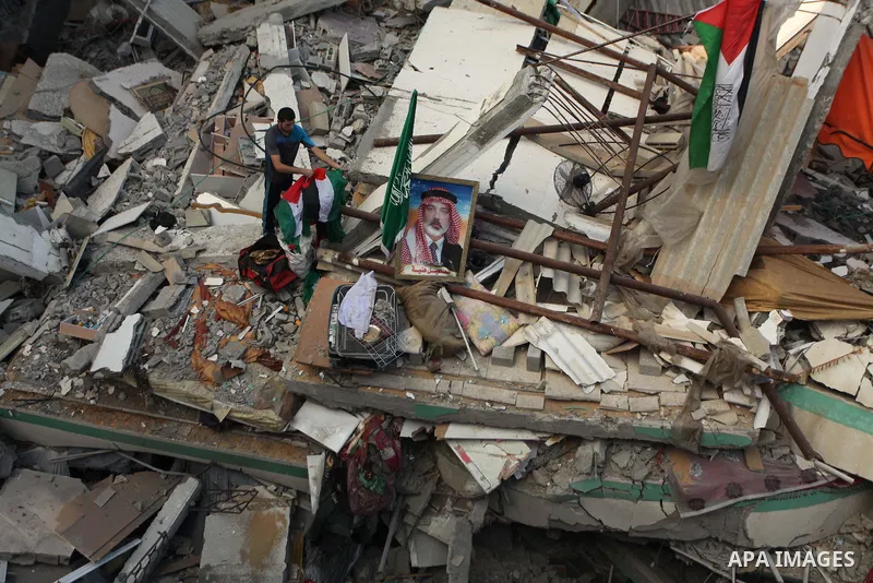 A Palestinian man displays national flags, Islamist Hamas movement flags and portraits of Hamas top leader in Gaza, Ismail Haniya, on the rubble of the latter's house after it was hit by an overnight Israeli air strike,...