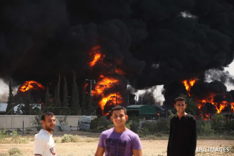 Palestinian men stand looking as flames engulf the fuel tanks of the only power plant supplying electricity to the Gaza Strip after it was hit by overnight Israeli shelling, on July 29, 2014, in the south of Gaza City. T...