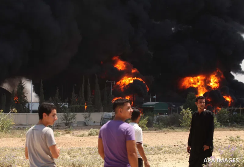 Palestinian men stand looking as flames engulf the fuel tanks of the only power plant supplying electricity to the Gaza Strip after it was hit by overnight Israeli shelling, on July 29, 2014, in the south of Gaza City. T...