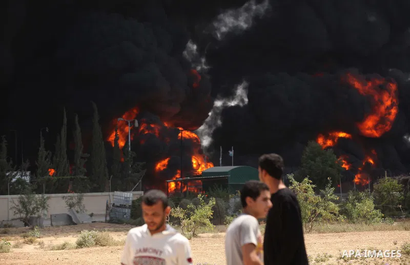 Palestinian men stand looking as flames engulf the fuel tanks of the only power plant supplying electricity to the Gaza Strip after it was hit by overnight Israeli shelling, on July 29, 2014, in the south of Gaza City. T...