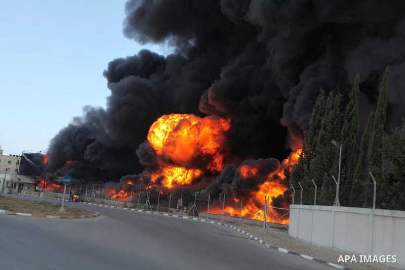 Palestinian men stand looking as flames engulf the fuel tanks of the only power plant supplying electricity to the Gaza Strip after it was hit by overnight Israeli shelling, on July 29, 2014, in the south of Gaza City. T...