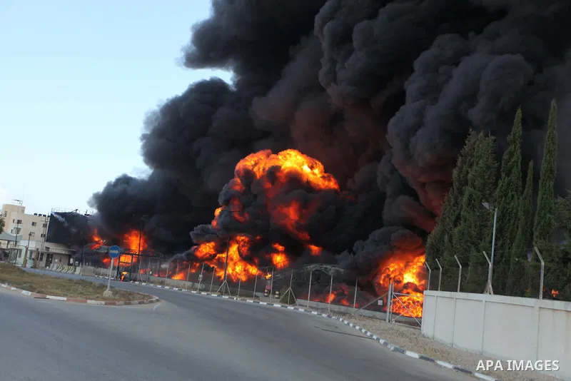 Palestinian men stand looking as flames engulf the fuel tanks of the only power plant supplying electricity to the Gaza Strip after it was hit by overnight Israeli shelling, on July 29, 2014, in the south of Gaza City. T...