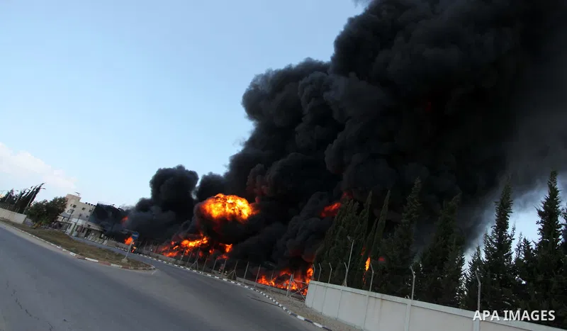 Palestinian men stand looking as flames engulf the fuel tanks of the only power plant supplying electricity to the Gaza Strip after it was hit by overnight Israeli shelling, on July 29, 2014, in the south of Gaza City. T...