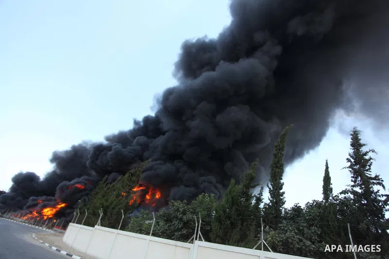 Palestinian men stand looking as flames engulf the fuel tanks of the only power plant supplying electricity to the Gaza Strip after it was hit by overnight Israeli shelling, on July 29, 2014, in the south of Gaza City. T...