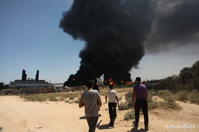 Palestinian men stand looking as flames engulf the fuel tanks of the only power plant supplying electricity to the Gaza Strip after it was hit by overnight Israeli shelling, on July 29, 2014, in the south of Gaza City. T...