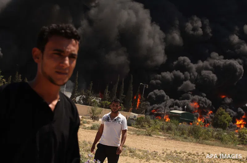 Palestinian men stand looking as flames engulf the fuel tanks of the only power plant supplying electricity to the Gaza Strip after it was hit by overnight Israeli shelling, on July 29, 2014, in the south of Gaza City. T...