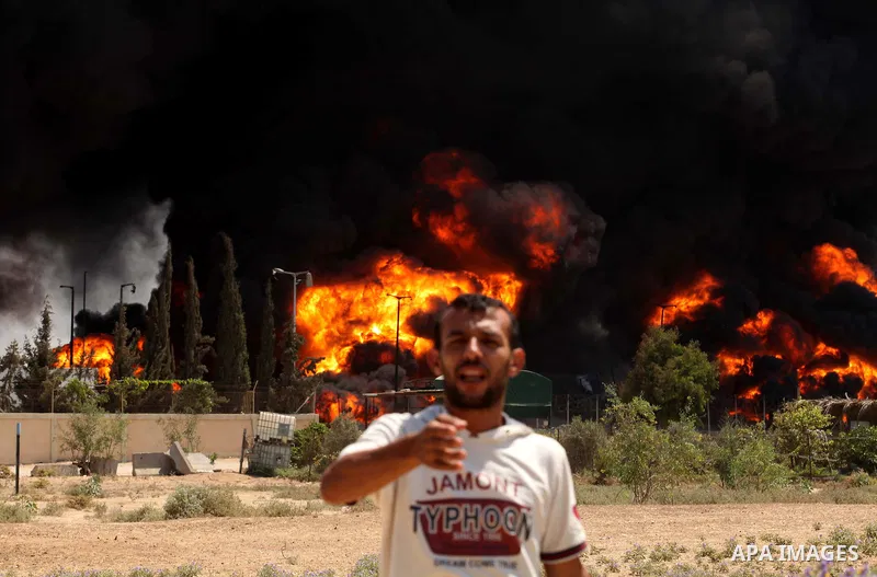 Palestinian men stand looking as flames engulf the fuel tanks of the only power plant supplying electricity to the Gaza Strip after it was hit by overnight Israeli shelling, on July 29, 2014, in the south of Gaza City. T...