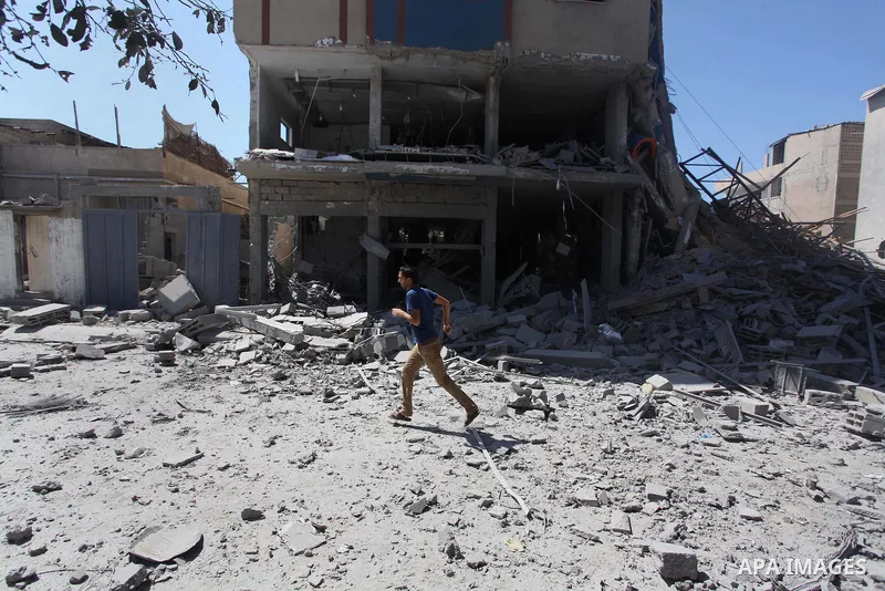 Palestinians walk past a building of Aqsa TV. destroyed by an Israeli air strike in Gaza city on July 31, 2014. Israel did not comment immediately on an incident on Wednesday, in nearby Shejaia, in which Palestinian offi...
