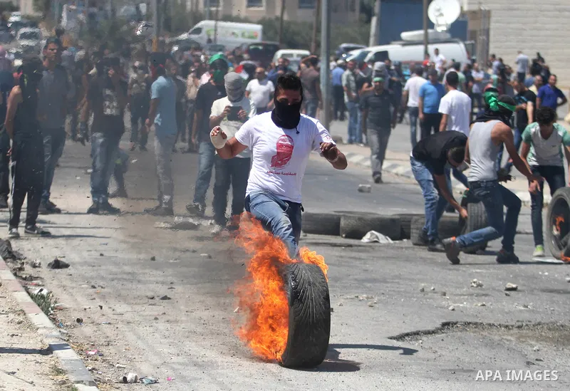 A Palestinian protester kicks a burning tyre during clashes with Israeli troops at a protest against the Israeli offensive in Gaza, outside Israel's Ofer military prison near the West Bank city of Ramallah August 1,2014....