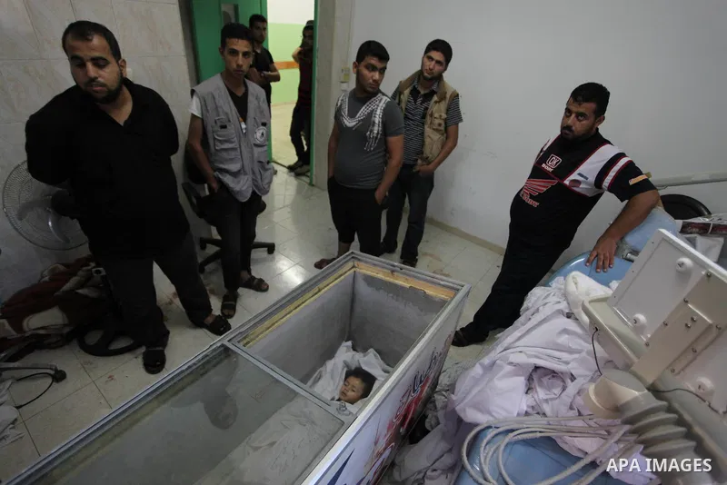 Palestinians gather around the body of two-and-a-half-year-old Palestinian girl Raghad Massoud, whom medics said was killed in an Israeli air strike, is seen inside an ice-cream freezer at Kuwaiti Hospital, which does no...
