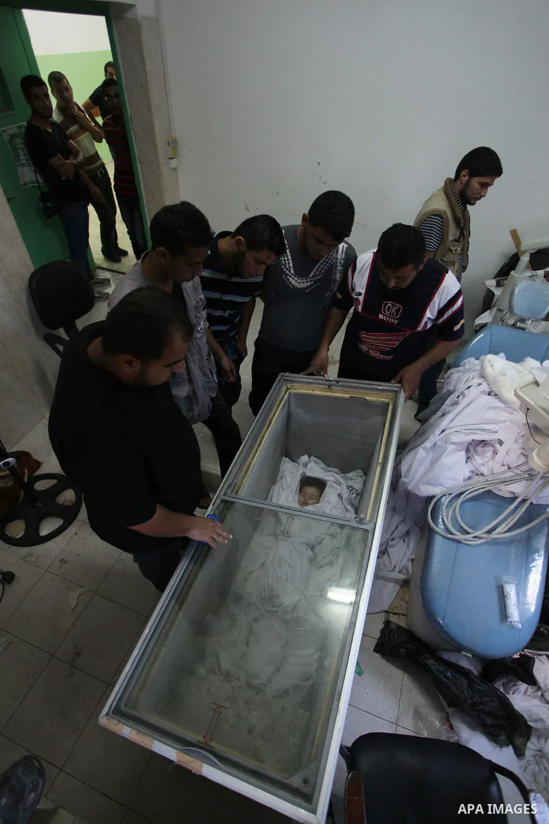 Palestinians gather around the body of two-and-a-half-year-old Palestinian girl Raghad Massoud, whom medics said was killed in an Israeli air strike, is seen inside an ice-cream freezer at Kuwaiti Hospital, which does no...