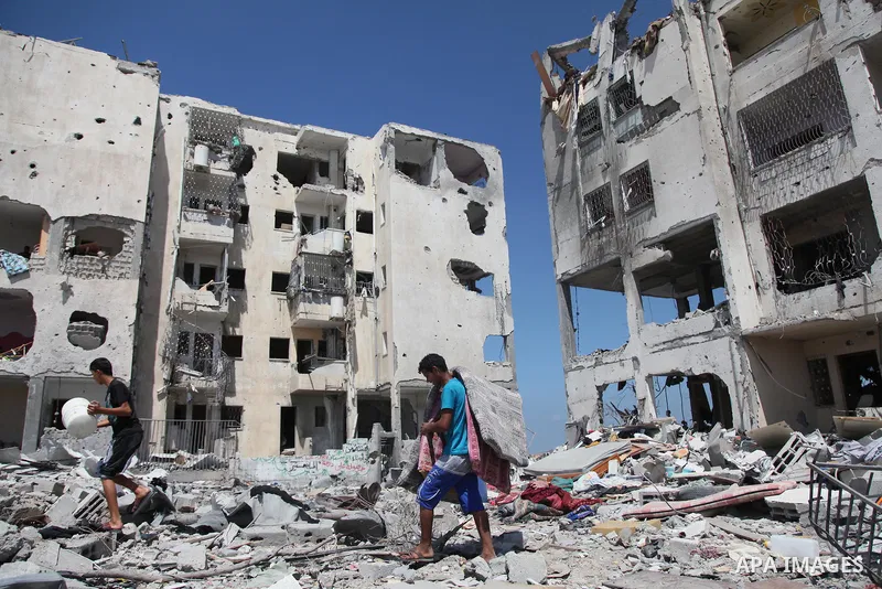Palestinians walk in front of the rubble of buildings destroyed in Israeli strikes, in Beit Lahiya, northern Gaza Strip, Monday, Aug. 4, 2014.. Photo by Ezz al-Zanoun