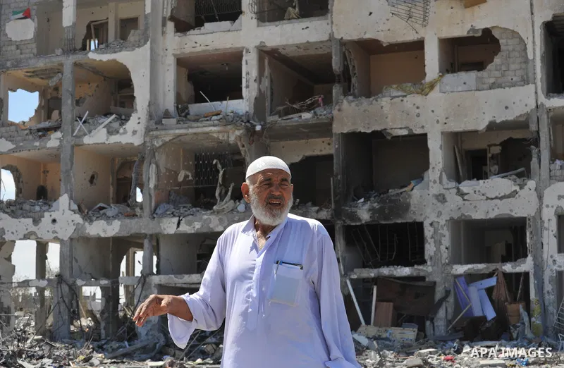 Palestinians walk in front of the rubble of buildings destroyed in Israeli strikes, in Beit Lahiya, northern Gaza Strip, Monday, Aug. 4, 2014.. Photo by Ezz al-Zanoun